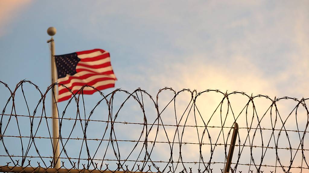 ARCHIV - Eine US-amerikanische Flagge weht hinter einem Stacheldrahtzaun im Wind. Foto: Maren Hennemuth/dpa