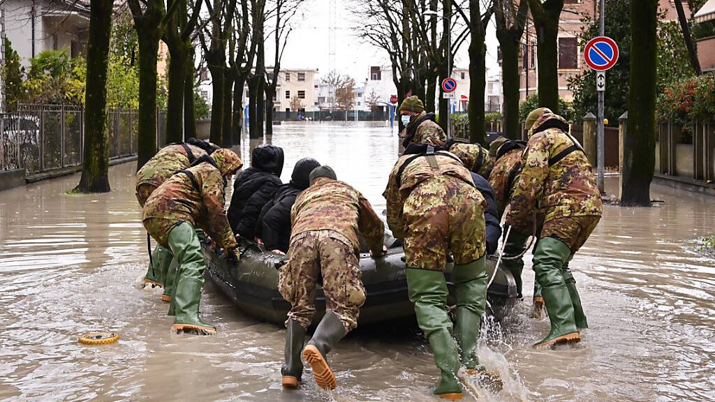 Männer schieben ein Boot inmitten einer überschwemmten Straße in einem Wohngebiet an. Die Wetterlage in Italien bleibt nach heftigen Niederschlägen vom Wochenende angespannt, etliche Familien mussten aus ihren Wohnungen evakuiert werden. Foto: Massimo Paolone/LaPresse via ZUMA Press/dpa