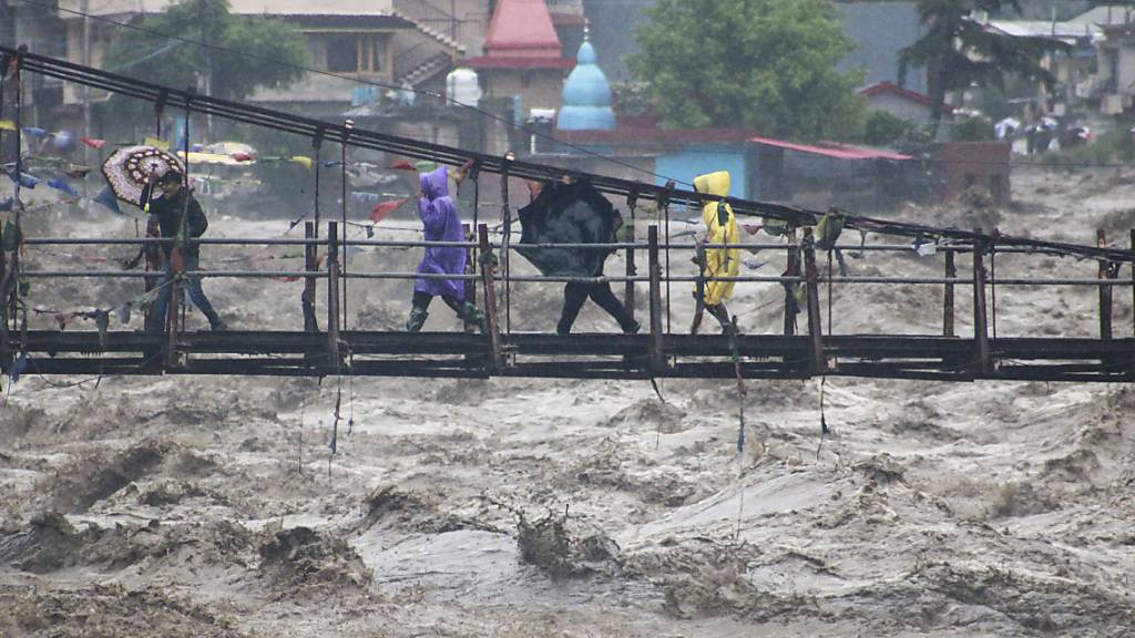Menschen gehen über eine Brücke, die über den Fluss Beas führt, der aufgrund starker Regenfälle angestiegen ist. Foto: Aqil Khan/AP/dpa