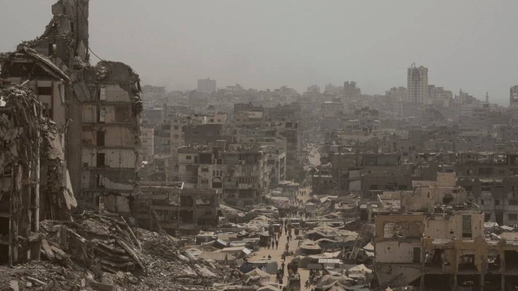 ARCHIV - Menschen gehen eine Straße entlang, die von Gebäuden umgeben ist, die durch israelische Bombardierungen im Gazastreifen zerstört wurden. Foto: Jehad Alshrafi/AP/dpa