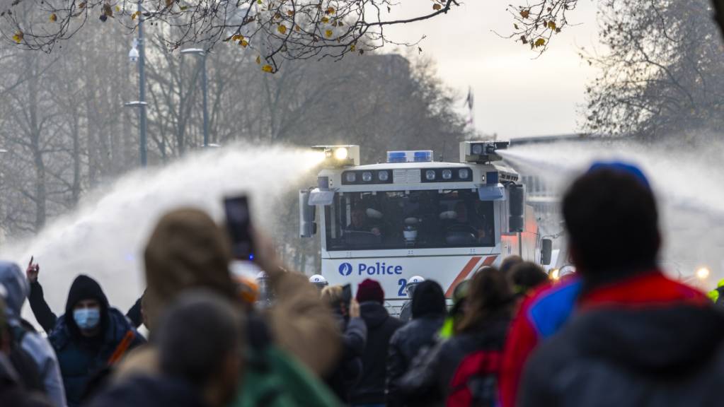 Protestteilnehmer filmen mit ihren Telefonen, wie die Polizei bei einem Zusammenstoss mit Demonstranten Wasserwerfern einsetzen. Nach Angaben der Polizei protestierten am Sonntag rund 35'000 Menschen in Brüssel gegen die verschärften Corona-Maßnahmen und insbesondere den Corona-Pass in Belgien.