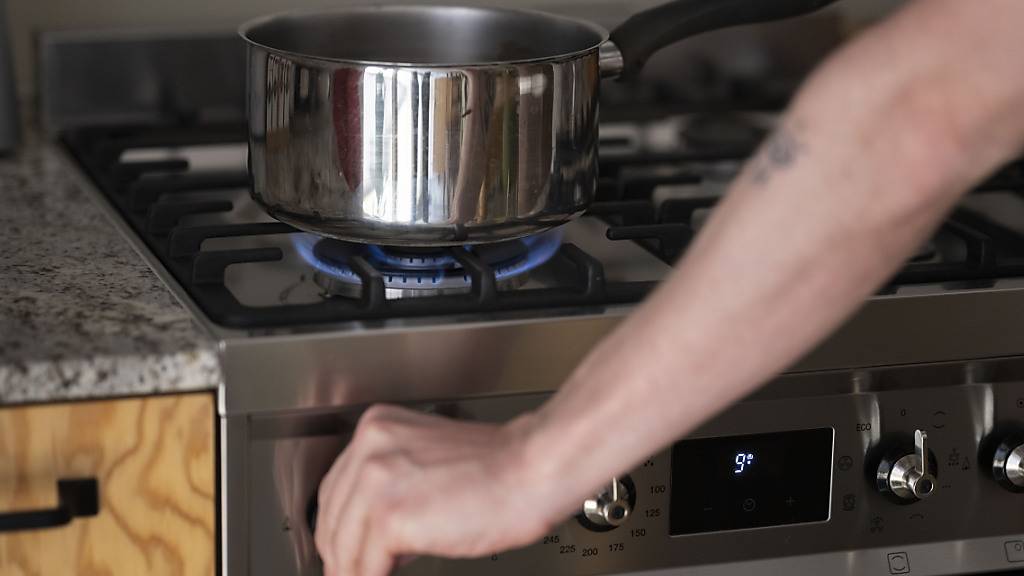 Ein Mann reguliert die Gasflamme eines Kochherds. (Archivbild)