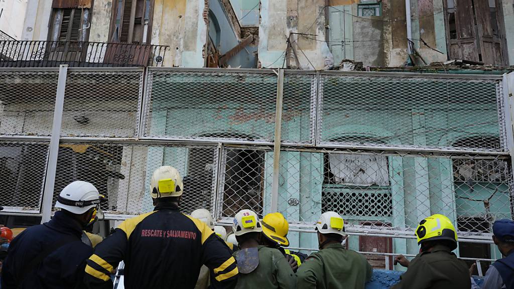 Feuerwehrleute beobachten ihre Kollegen bei der Suche nach Überlebenden, nachdem ein Wohnhaus in der berühmten kubanischen Altstadt teils in sich zusammen gefallen ist. Nach offiziellen Angaben lebten in dem dreistöckigen Gebäude 13 Familien von insgesamt 54 Menschen. Foto: Ramon Espinosa/AP/dpa