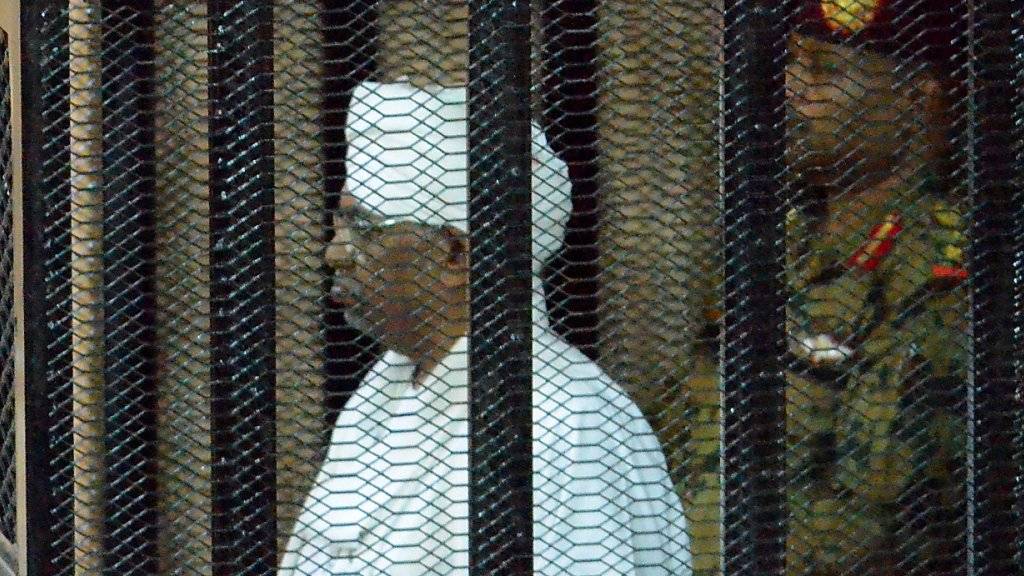 Der in eine weisse sudanesische Robe gekleidete angeklagte frühere Machthaber Sudans, Omar al-Baschir, verfolgt den Prozess aus einem Gitterkäfig im Gerichtssaal.