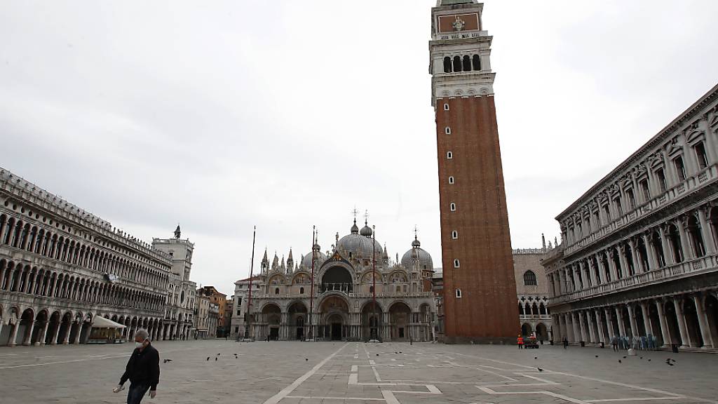 ARCHIV - Ein Mann geht über den leeren Markusplatz in Venedig - Touristen bleiben auch hier vorerst aus. Foto: Antonio Calanni/AP/dpa