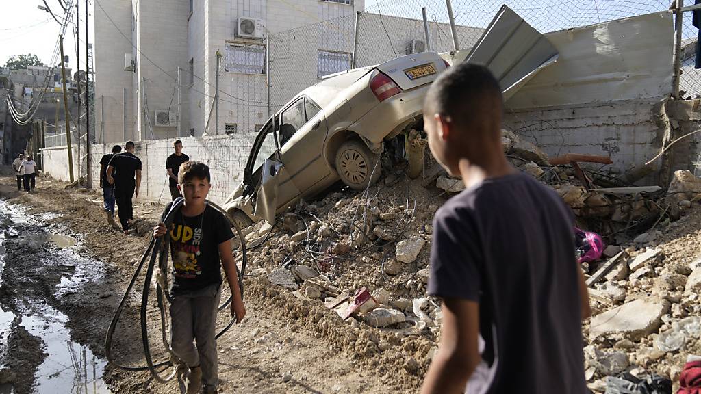 Palästinensische Flüchtlinge gehen nach einer Militäroperation der israelischen Armee an einem beschädigten Fahrzeug im Flüchtlingslager im Westjordanland vorbei. Foto: Nasser Nasser/AP/dpa