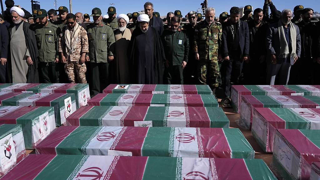 dpatopbilder - Trauernde beten neben den mit Fahnen bedeckten Särgen während einer Trauerzeremonie für die Anschlagsopfer am vierten Todestag des iranischen Generals Ghassem Soleimani in der Stadt Kerman. Foto: Vahid Salemi/AP/dpa