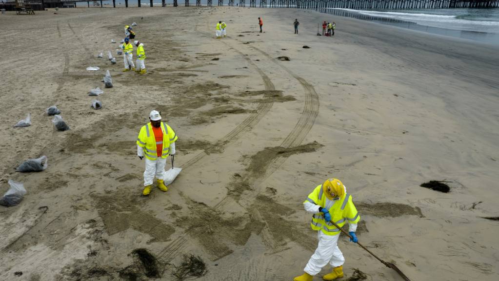 Arbeiter in Schutzanzügen säubern einen vom ausgetretenen Öl verunreinigten Strand in Newport Beach in Kalifornien. Foto: Ringo H.W. Chiu/AP/dpa