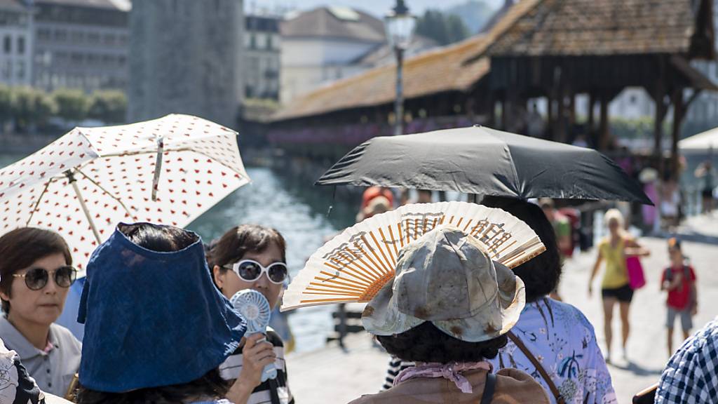 Touristen aus Asien trotzen der Hitze vor der Kapellbruecke in der Stadt Luzern am Dienstag, 22. August 2023. (KEYSTONE/Urs Flueeler).