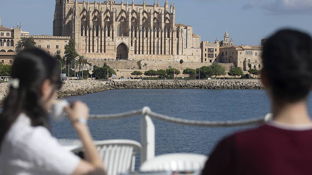 ARCHIV - An einem sonnigen Tag in Palma nehmen zwei Personen gegenüber der Kathedrale von Palma einen Drink auf der Terrasse eines Restaurants. Foto: Clara Margais/dpa