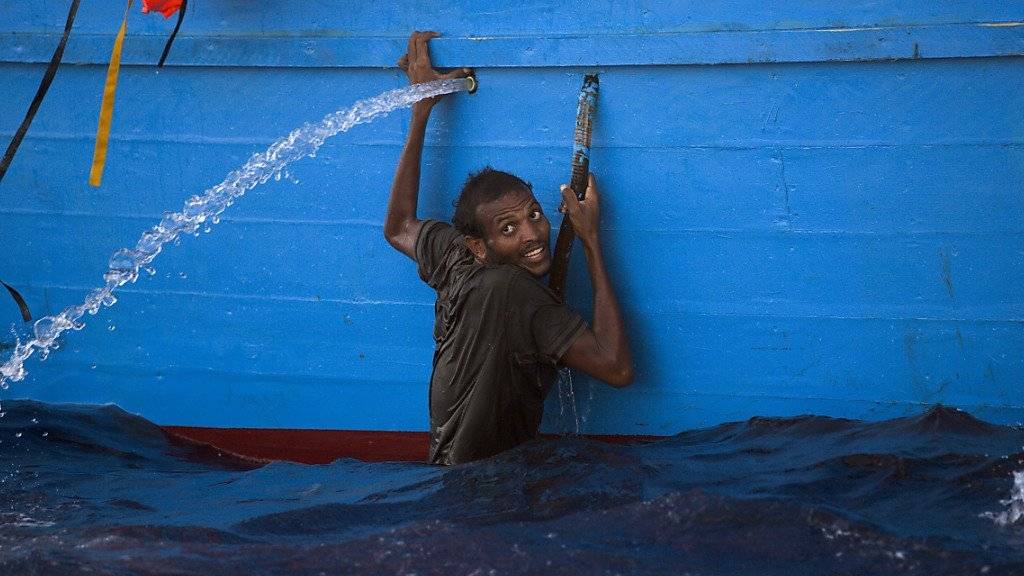 Ein Mann klammer sich an ein Boot im Meer vor Libyen, wo die italienische Küstenwache rund 6500 Flüchtlinge aus Seenot rettete.
