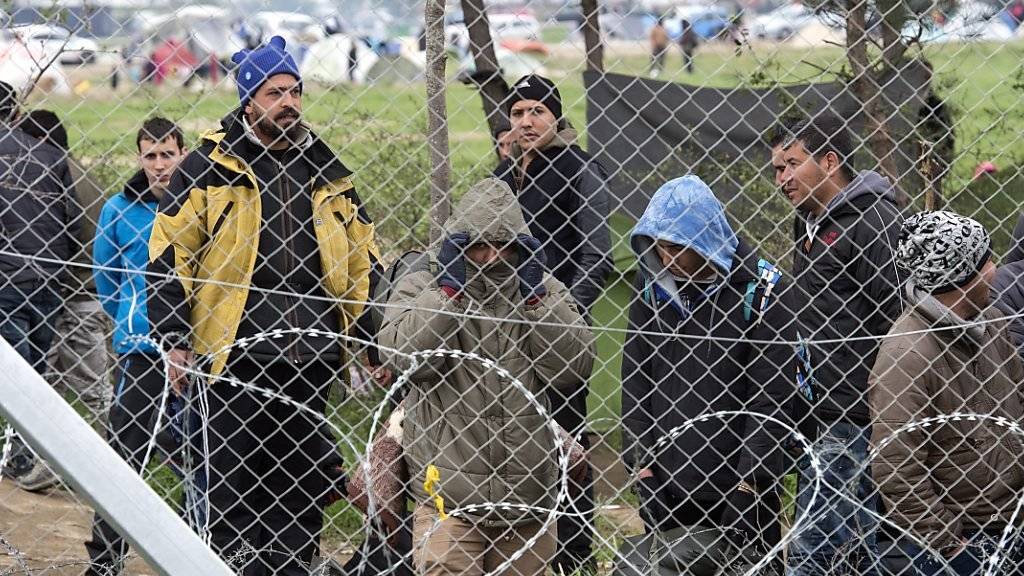 Flüchtlinge warten hinter einem Zaun an der griechisch-mazedonischen Grenze.