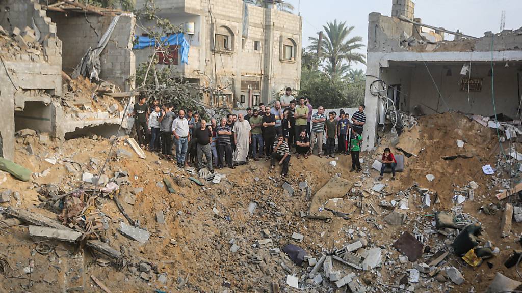 Palästinenser stehen um einen Krater herum, der durch einen israelischen Angriff verursacht wurde. Foto: Mohammed Talatene/dpa
