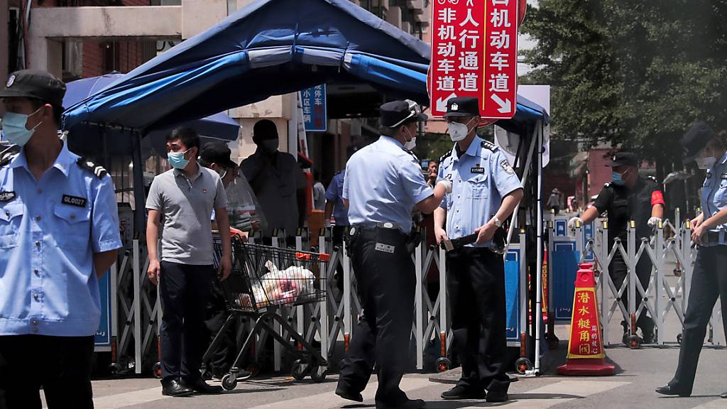 Polizeibeamte und Sicherheitsbeamte, die Schutzmasken tragen, stehen vor Wohngebäuden Wache, die nach einem positiven Fall auf einem nahe gelegenen Markt abgeriegelt wurden. Foto: Andy Wong/AP/dpa