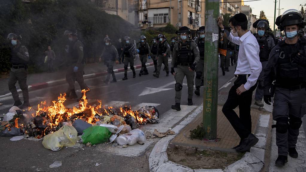 Polizisten gehen während einer Demonstration von ultraorthodoxen Juden auf einer Straße an brennendem Müll vorbei. Foto: Oded Balilty/AP/dpa