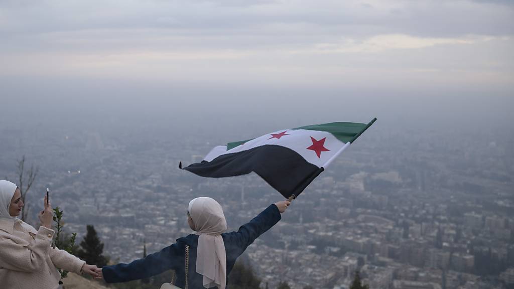 ARCHIV - Eine junge Frau posiert für ein Foto mit einer Flagge der syrischen Opposition an einem Aussichtspunkt auf dem Berg Qasiyun oberhalb der Stadt Damaskus. Foto: Leo Correa/AP/dpa