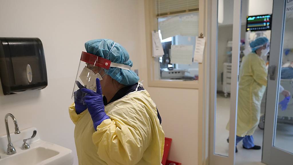 Eine Pflegehelferin Lori Pond (l) legt ihre Schutzkleidung ab, nachdem sie das Zimmer eines Patienten in der Corona-Intensivstation verlassen hat. Die den USA sind in der Coronavirus-Pandemie so viele Krankenhausbetten belegt wie nie zuvor. Das teilte das Gesundheitsministeriums am Dienstag mit.