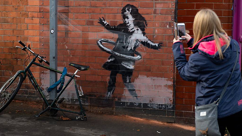 Corona und der Umgang mit der Krise - auch in  den Kunstwerke von Banksy spiegeln sich die Herausforderungen dieses Jahres deutlich wieder: In Nottingham tauchte etwa an einer Hauswand ein Bild eines Mädchen auf, dass mit einem Fahrradreifen Hula-Hoop spielt. Foto: Jacob King/PA Media/dpa - ACHTUNG: Nur zur redaktionellen Verwendung im Zusammenhang mit der aktuellen Berichterstattung.
