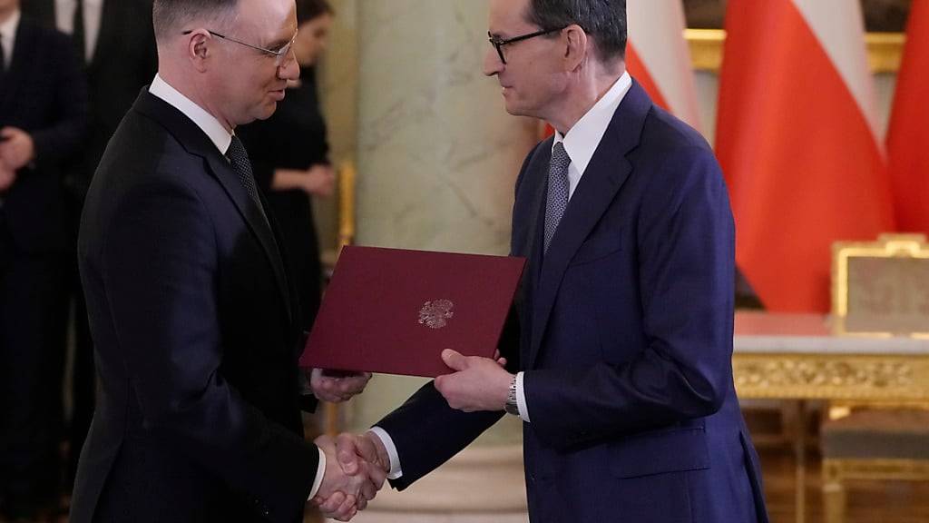 Polens Präsident Andrzej Duda (l) und Polens Ministerpräsident Mateusz Morawiecki geben sich während einer Vereidigungszeremonie in Warschau die Hand. Foto: Czarek Sokolowski/AP/dpa