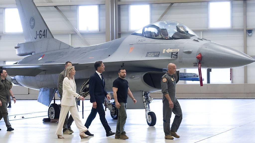 Ukraines Präsident Wolodymyr Selenskyj (2.v.r) und Niederlandes Ministerpräsident Mark Rutte (M) laufen an einem  F-16 Kampfjet vorbei. Foto: Peter Dejong/AP/dpa