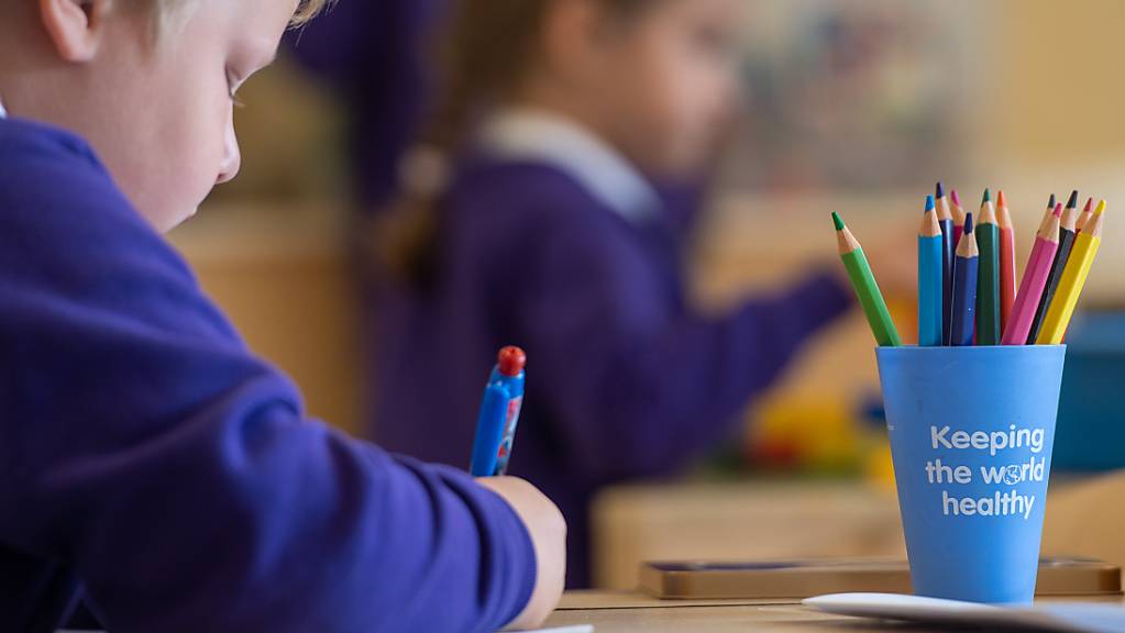 Ein Schüler sitzt an einem Tisch in einem Klassenzimmer der Grundschule «Queen's Hill Primary School», vor ihm steht ein Stiftebecher mit der Aufschrift «Keeping the world healthy».