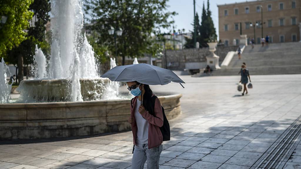 Eine Frau schützt sich bei Temperaturen über 40 Grad auf dem Syntagma-Platz in Athen mit einem Schirm vor Sonne und Hitze. Foto: Angelos Tzortzinis/dpa