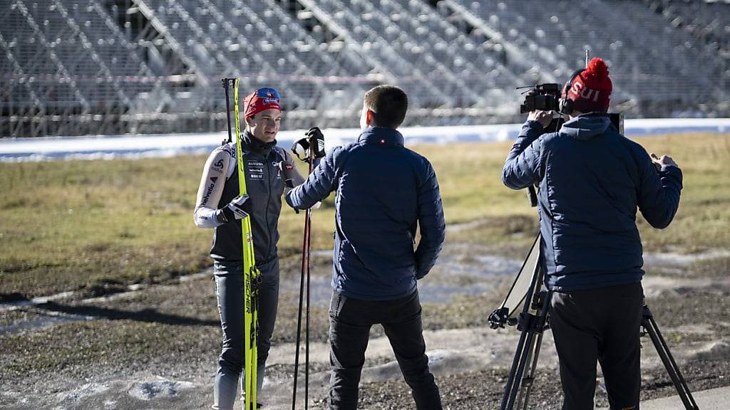 Niklas Hartweg gibt in Lenzerheide Auskunft zum Saisonstart, während im Hintergrund bereits die Bauten für die Biathlon-WM erstellt werden