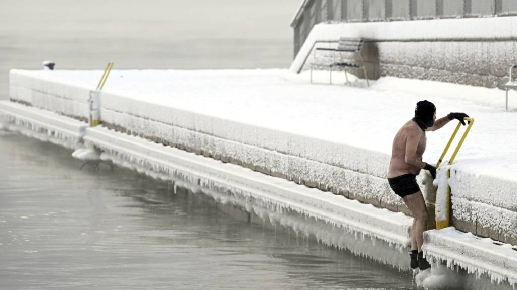 Ein Mann klettert aus dem eisigen Meer auf den Pier. Finnland und Schweden haben am Dienstag die Kälterekorde dieses Winters aufgestellt, als die Temperaturen in der nordischen Region auf über minus 40 Grad sanken. Foto: Vesa Moilanen/Lehtikuva/AP/dpa