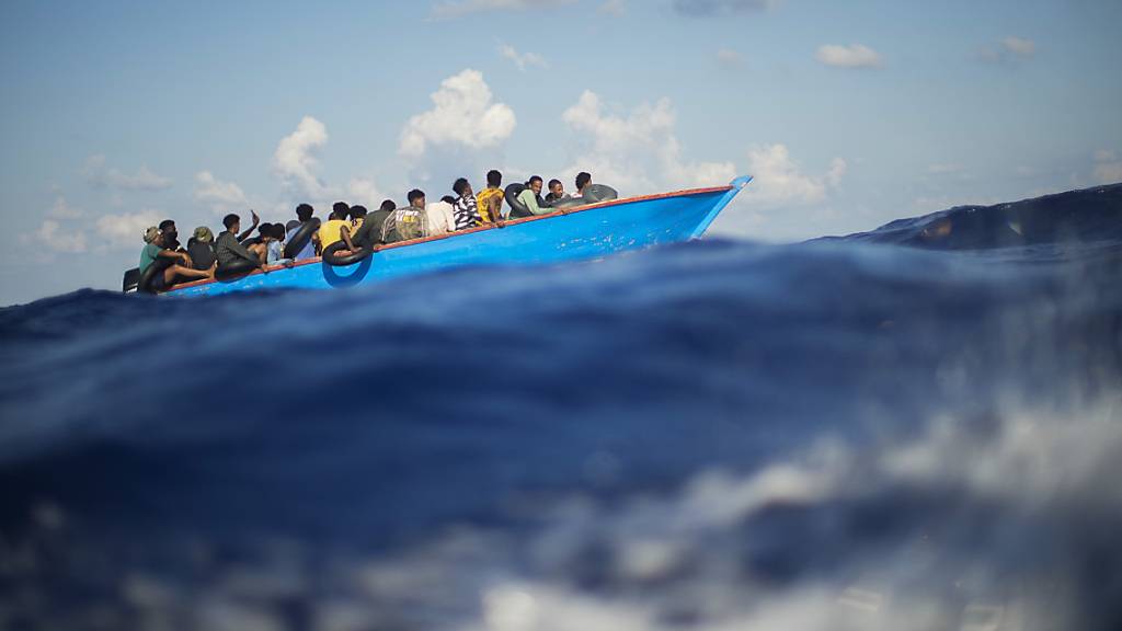 ARCHIV - Migranten sitzen in einem Holzboot im Mittelmeer nahe der Insel Lampedusa. (Archiv) Foto: Francisco Seco/AP/dpa
