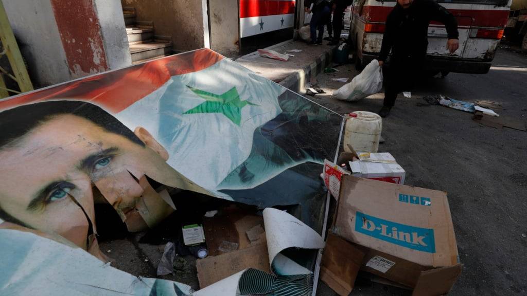 ARCHIV - Ein syrisches Mitglied der Rebellen bereitet sich darauf vor, Drogen und alkoholische Getränke zu vernichten, die in einem Gebäudekomplex gefunden wurden, während er an einem beschädigten Banner vorbeigeht, auf dem der gestürzte syrische Präsident Assad abgebildet ist. Foto: Omar Sanadiki/AP/dpa (Archivbild)