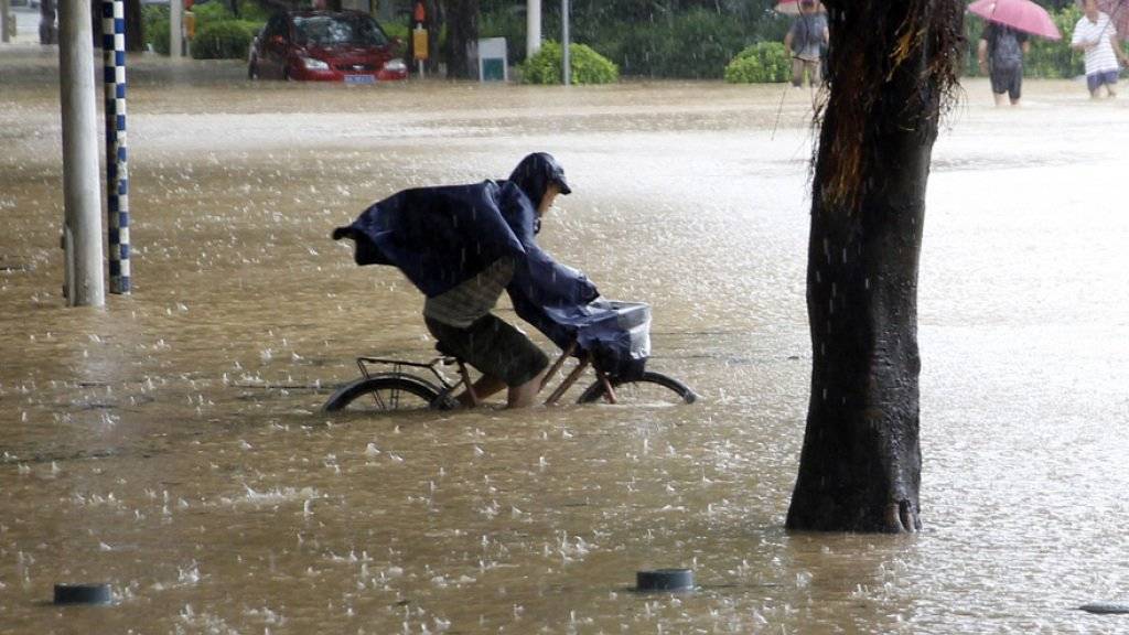 Ein Mann fährt mit seinem Fahrrad durch eine überschwemmte Strasse im Südosten Chinas.