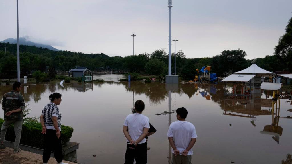 Menschen betrachten einen Park, der nach heftigen Regenfällen im Bezirk Miyun am Stadtrand von Peking, China, überflutet ist. Foto: Mahesh Kumar A./AP/dpa