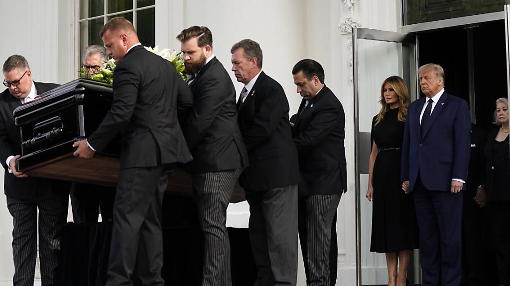 US-Präsident Donald Trump und First Lady Melania Trump stehen nebeneinander, während der Sarg von Robert Trump nach einer Gedenkfeier im Weißen Haus in einen Leichenwagen geladen wird. Foto: Evan Vucci/AP/dpa