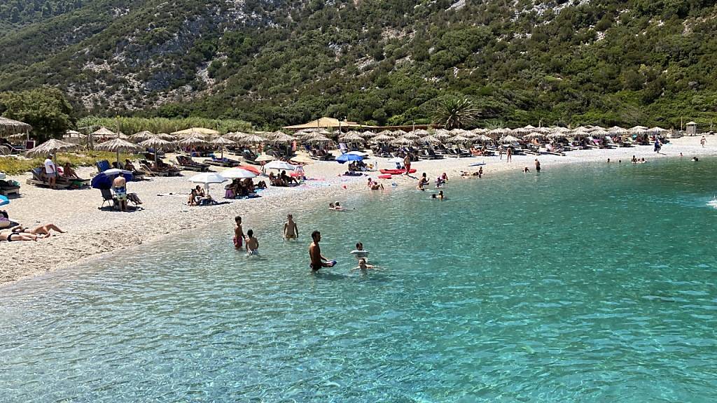 Menschen verbringen den heißen Sommertag an einem Strand auf der Sporaden-Insel Skopelos. Foto: Alexia Angelopoulou/dpa
