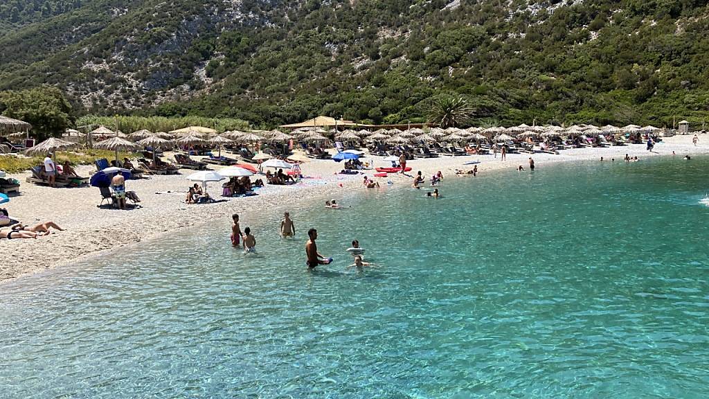 Menschen verbringen den heißen Sommertag an einem Strand auf der Sporaden-Insel Skopelos. Foto: Alexia Angelopoulou/dpa
