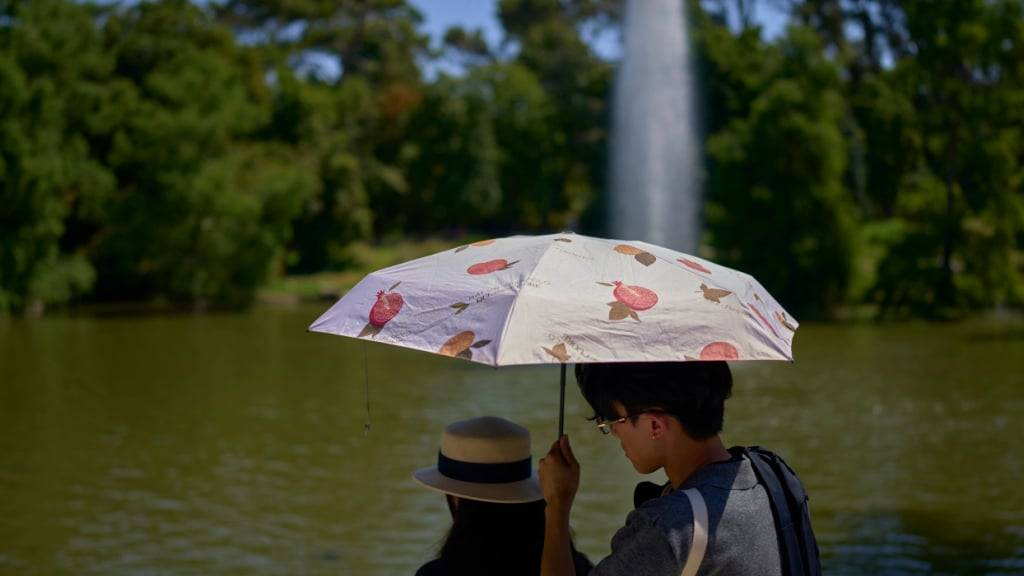Ein Paar schützt sich bei heißem Wetter mit einem Regenschirm in Madrid vor der Sonne. Foto: Manu Fernandez/AP/dpa