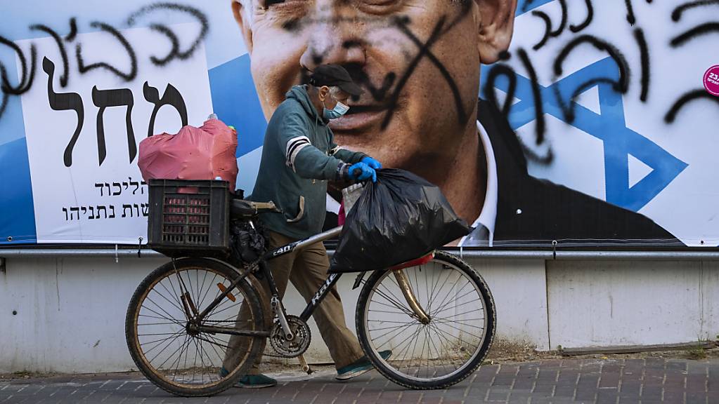 Ein Mann schiebt ein Fahrrad an einem beschmierten Wahlkampfplakat der Likud-Partei mit dem Bild des Parteivorsitzenden und Israels Ministerpräsidenten Netanjahu vorbei. Foto: Oded Balilty/AP/dpa