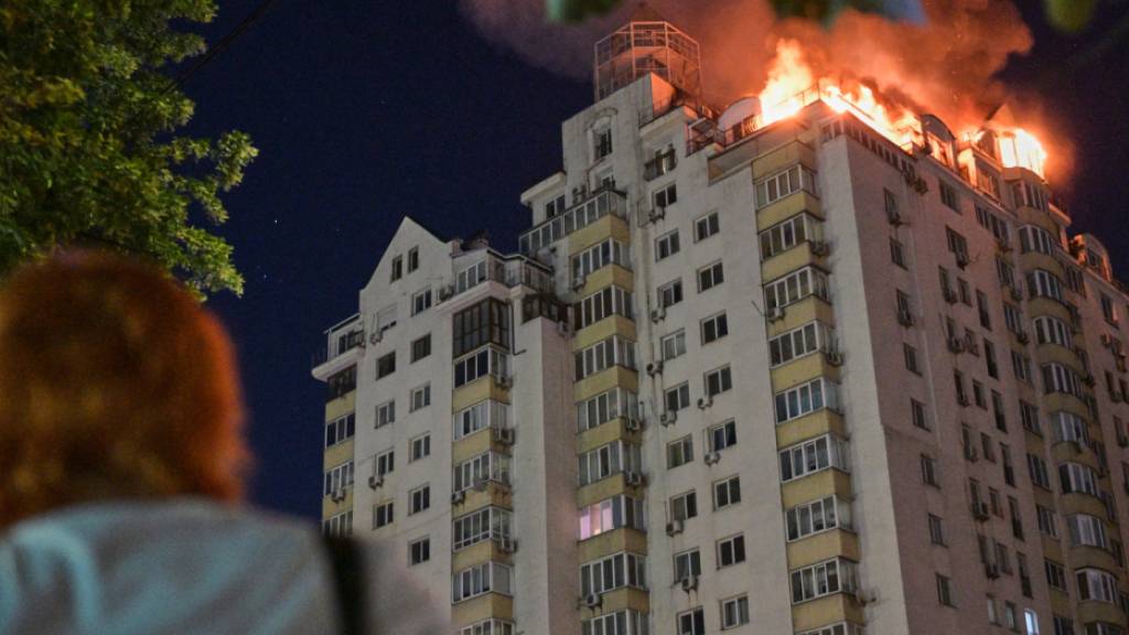 Eine Frau blickt auf ein Wohnhaus, das nach einem russischen Raketenangriff in Flammen steht. Foto: Danylo Antoniuk/AP/dpa