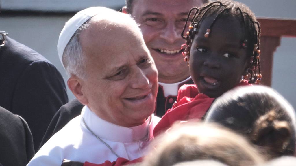 Papst Leo XIV. h‰lt ein kleines M‰dchen im Arm, als er zu einem Treffen mit Migranten im Aufnahmezentrum Las RaÌces in San CristÛbal de La Laguna auf Teneriffa eintrifft. Foto: Arturo Rodriguez/AP/dpa