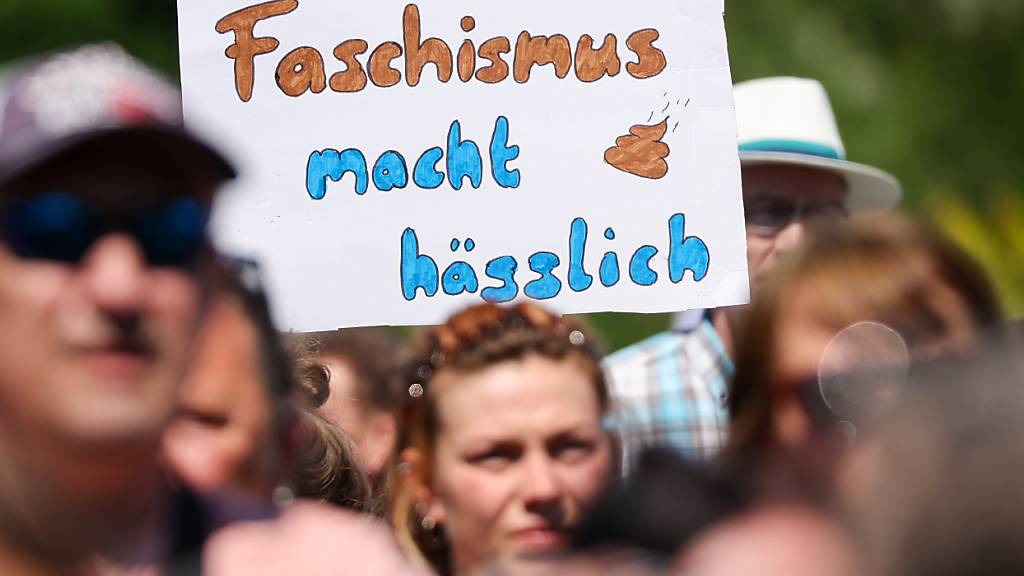 Ein Schild «Faschismus macht hässlich» hält ein Teilnehmer der Kundgebung «Hand in Hand für Demokratie und Menschenrechte» gegen Rechtsextremismus auf dem Leuschnerplatz in die Höhe. Foto: Jan Woitas/dpa