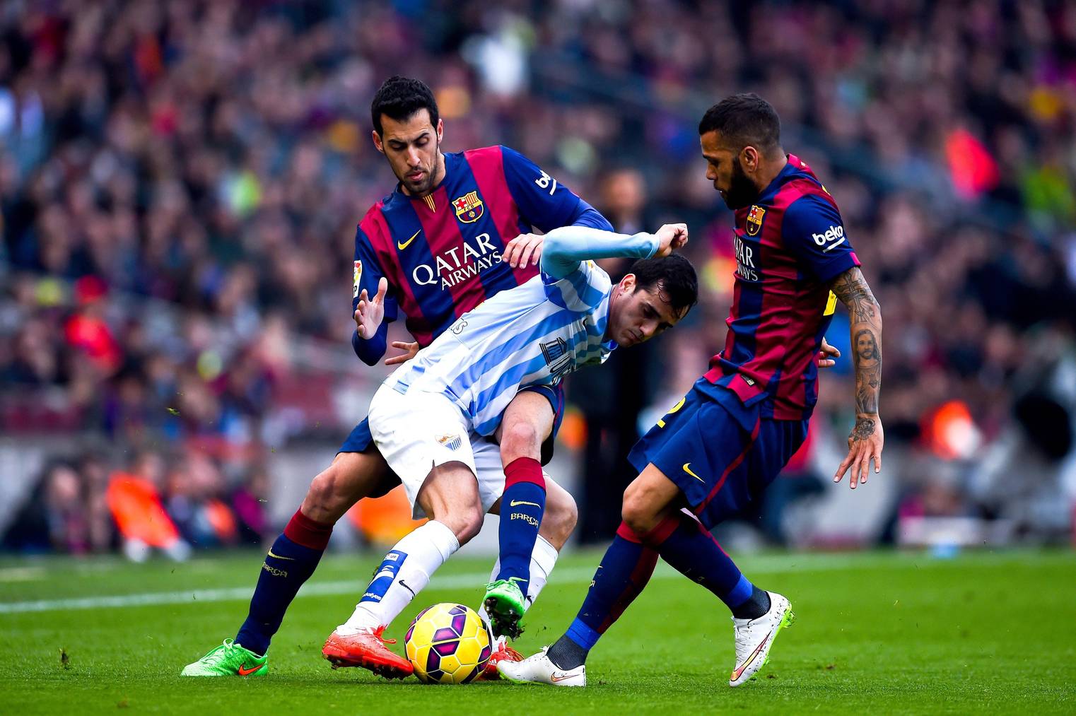 BARCELONA, SPAIN - FEBRUARY 21:  Juanmi Jimenez of Malaga CF competes for the ball with Sergio Busquets and Dani Alves of FC Barcelona during the La Liga match between FC Barcelona and Malaga CF at Camp Nou on February 21, 2015 in Barcelona, Spain.  (Photo by David Ramos/Getty Images)