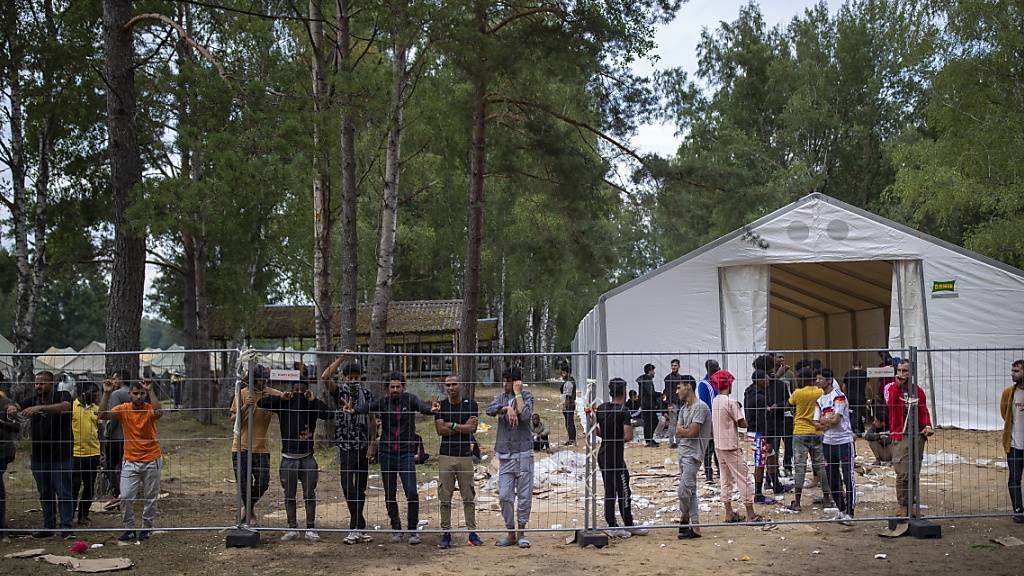 Geflüchtete stehen hinter einem Zaun des neu errichteten Flüchtlingslagers auf dem Truppenübungsplatz Rudninkai, etwa 38 km südlich von Vilnius. Das Rote Kreuz kritisierte die Entscheidung der litauischen Regierung, Migranten aus Belarus abzuweisen und erinnert daran, dass dies nicht völkerrechtlich vereinbar ist. In Litauen nahm in letzter Zeit die Zahl von Migranten zu, die über Belarus einreisen. Foto: Mindaugas Kulbis/AP/dpa