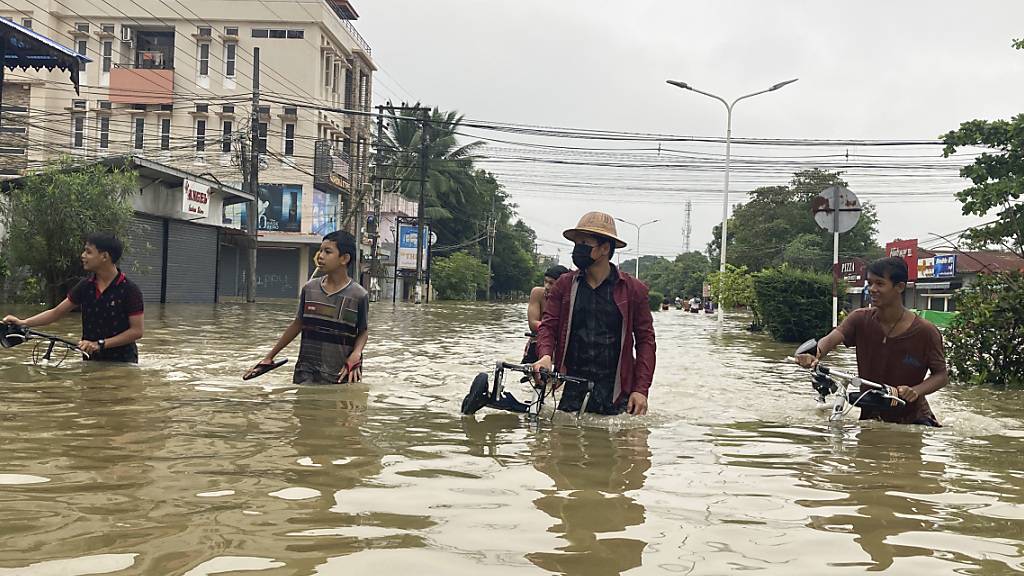 Bewohner von Bago schieben Fahrräder durch eine überschwemmte Straße. Foto: Thein Zaw/AP/dpa