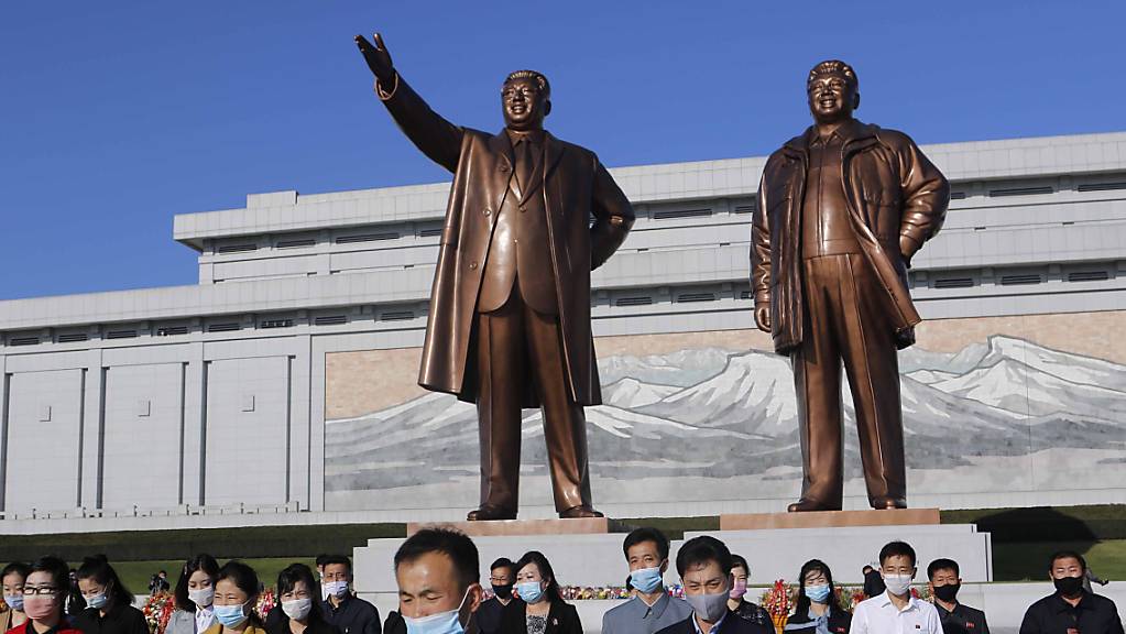 Menschen mit Maske besuchen den Mansu-Hügel, um vor dem Grossmonument Mansudae, welches die zwei verstorbenen nordkoreanischen Machthaber Kim Il-sung (l) und Kim Jong-il zeigt, anlässlich des 75. Jahrestages der Gründung der Arbeiterpartei des Landes, Blumen niederzulegen. Foto: Cha Song Ho/AP/dpa