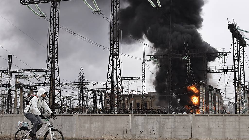ARCHIV - Ein Mann radelt nach einem russischen Angriff an einem Elektrizitätswerk in Charkiw vorbei. Foto: Yevhen Titov/AP/dpa