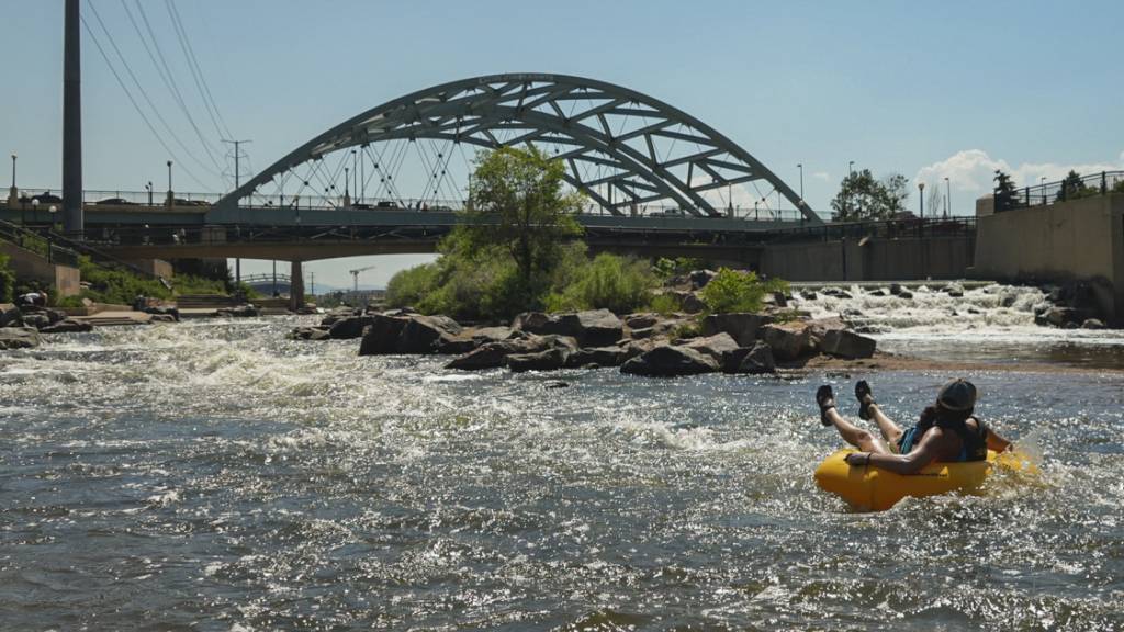 Menschen kühlen sich im Wasser ab, am Zusammenfluss von South Platte River und Cherry Creek. Am Nachmittag erreichte die Temperatur 35 Grad Celsius als Teil der Hitzewelle, die über den Westen der USA hinwegfegt. Foto: Brittany Peterson/AP/dpa