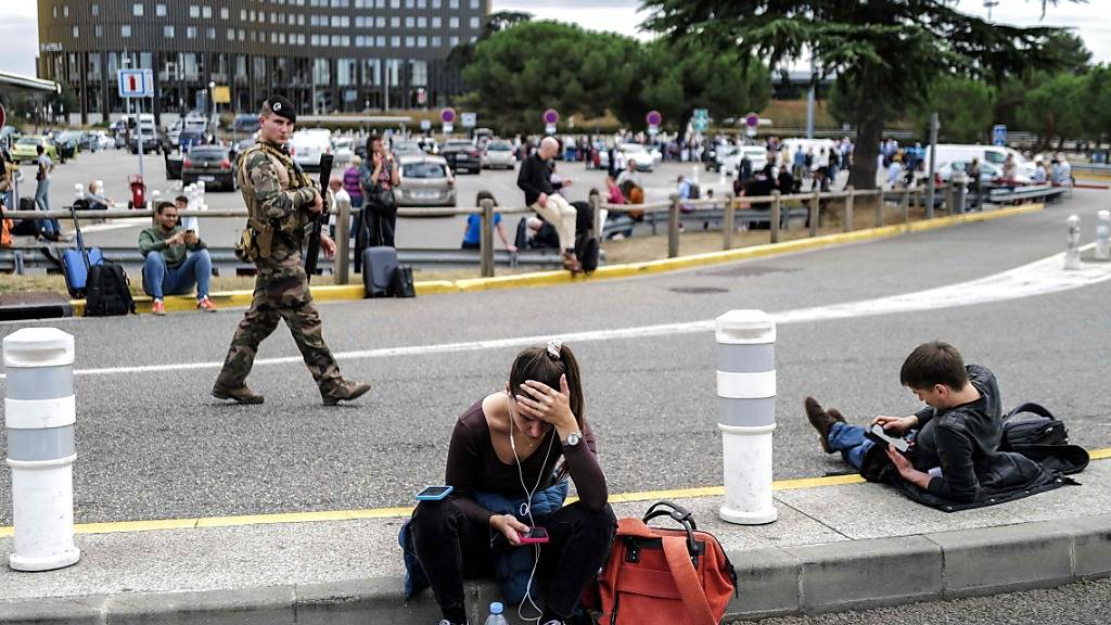Reisende warten nach einer Bombendrohung vor dem Flughafen Toulouse-Blagnac, während ein französischer Soldat patrouilliert. Foto: Charly Triballeau/AFP/dpa