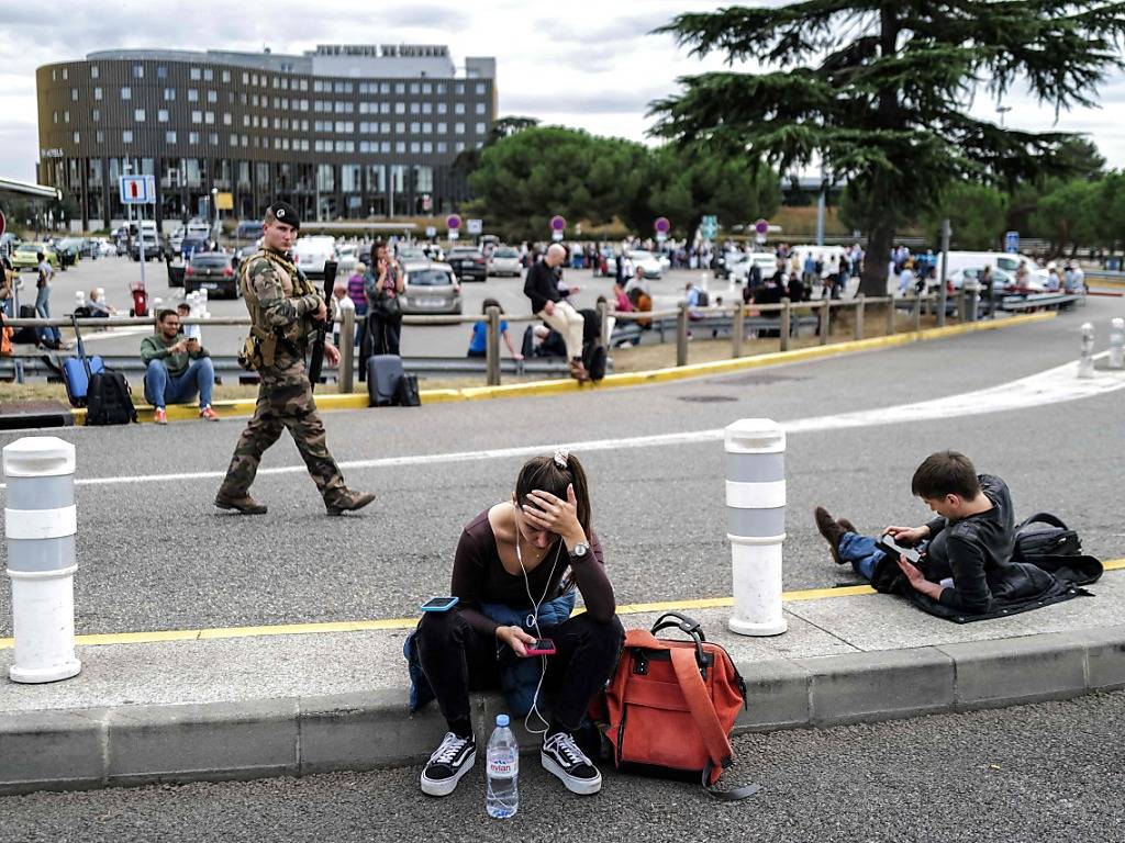 Reisende warten nach einer Bombendrohung vor dem Flughafen Toulouse-Blagnac, während ein französischer Soldat patrouilliert. Foto: Charly Triballeau/AFP/dpa