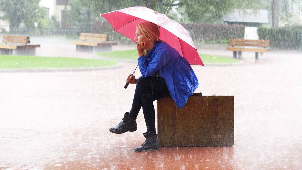 Frau sitzt mit Regenschirm im Regen (Symbolbild).