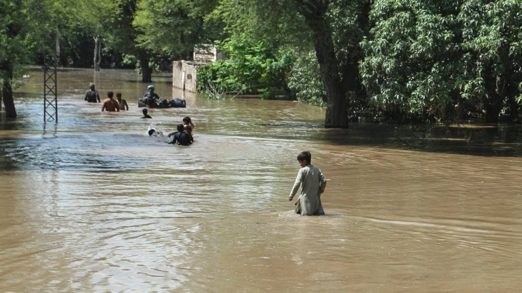 Dorfbewohner waten durch ein überschwemmtes Gebiet. Foto: Asim Tanveer/AP/dpa